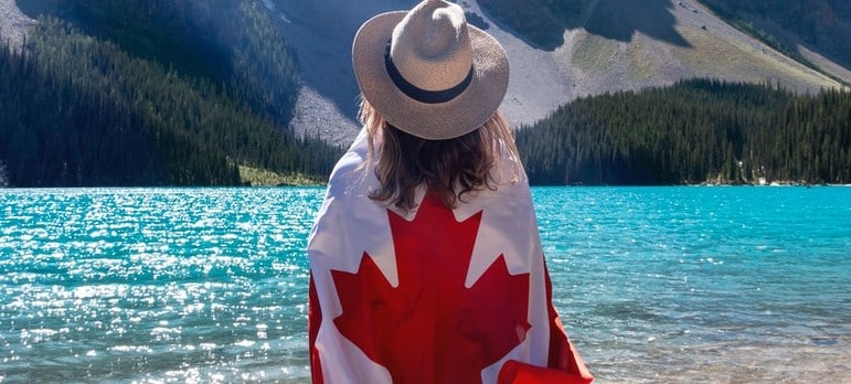 person with a Canadian flag around her standing near a lake