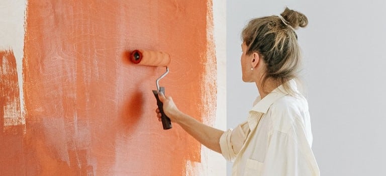 Painting walls like the woman in the photo is one of the best home improvements to make before selling