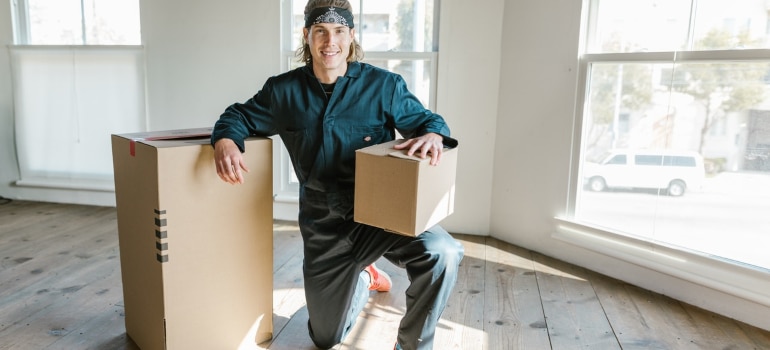 a man in blue overalls posing with two cardboard boxes in an empty home