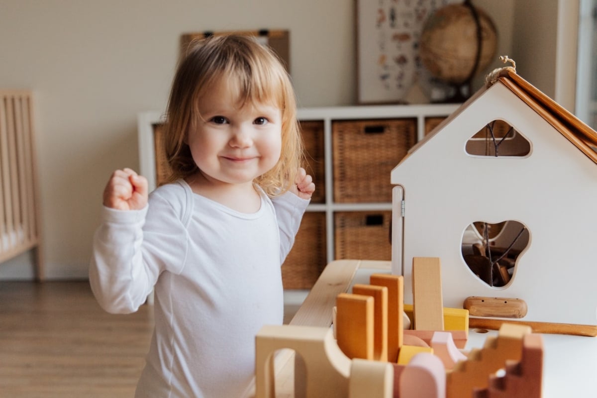 Little girl playing with wooden house in her room