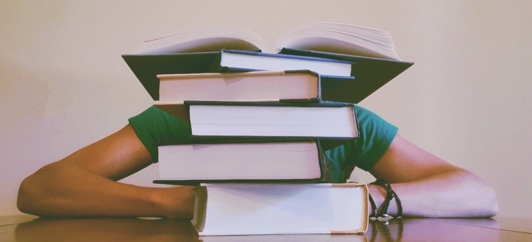 a student behind a pile of books on a table