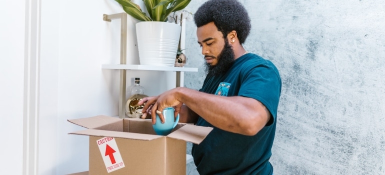 a mover packing a blue cup into a cardboard box while preparing the client for leaving Ontario