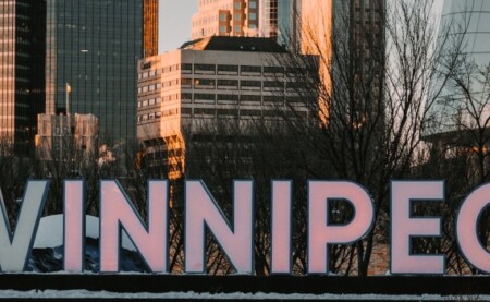 a park in the city of Winnipeg showing the name of the city with buildings behind it