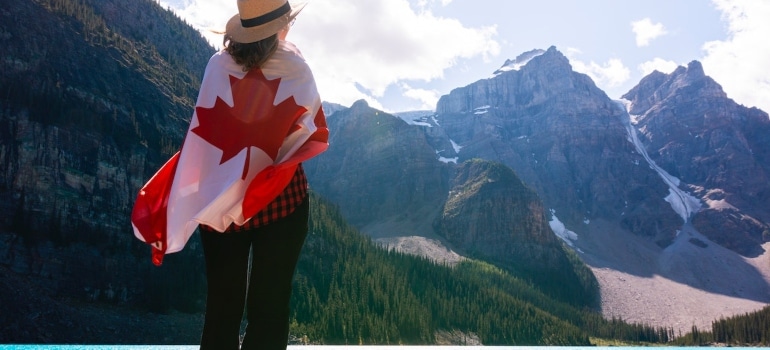 a woman wrapped in a Canadian flag looking at the distant and thinking of moving to a new province in Canada