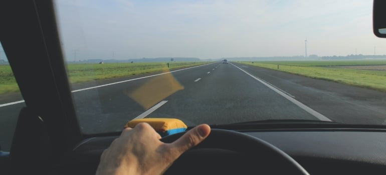 a person's hand resting on the steering wheel while on an open road