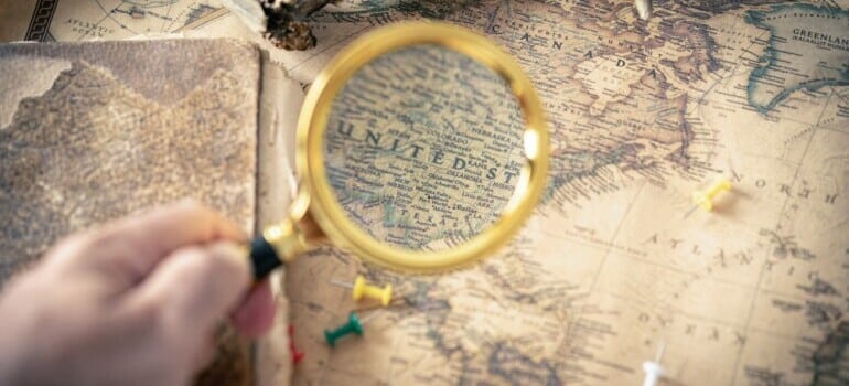 person using magnifying glass on US map and thinking of moving from Toronto to Seattle