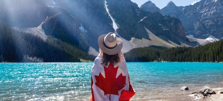 woman with Canadian flag by the lake thinking about moving to one of the best provinces for families