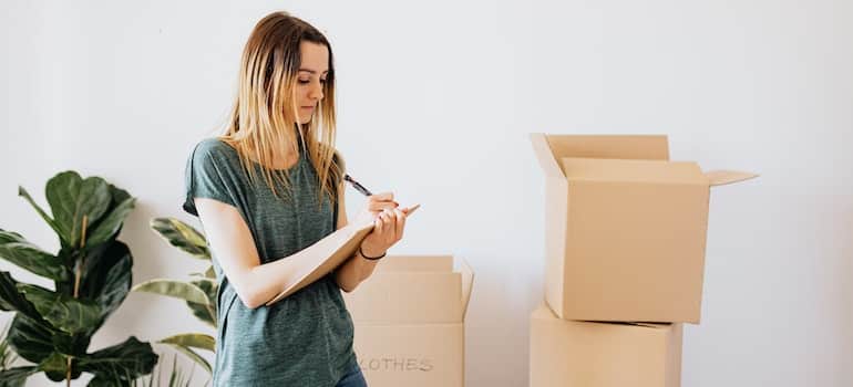 woman taking notes while packing boxes