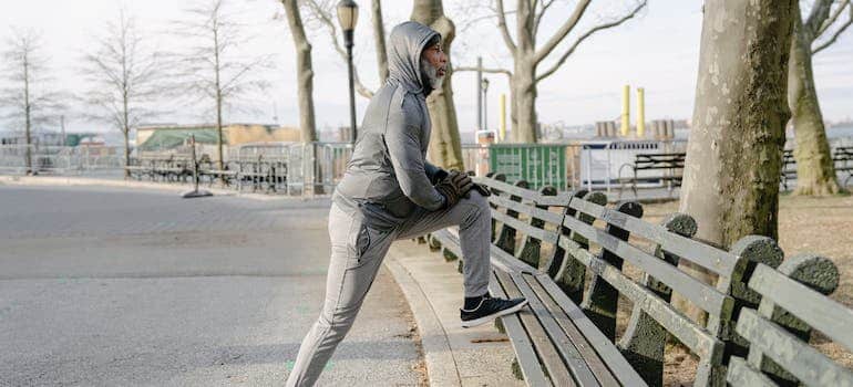Old black man in sportswear stretching legs in park
