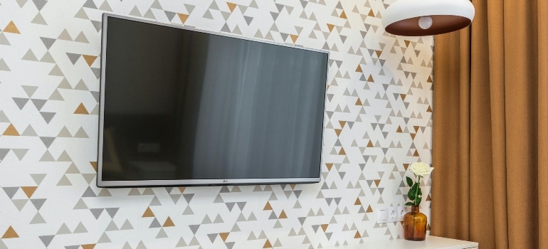 Mounted flat screen TV on a patterned wall with curtains and a lamp—perfect example for how to move a flat screen TV securely.