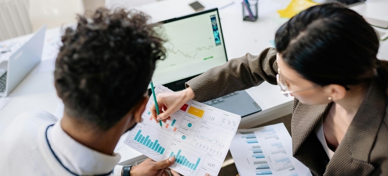 Two professionals reviewing colorful bar and pie charts during a business meeting.