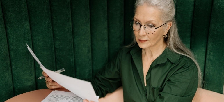Elderly woman with eyeglasses reading a contract related to Buying a home in Brandon MB.