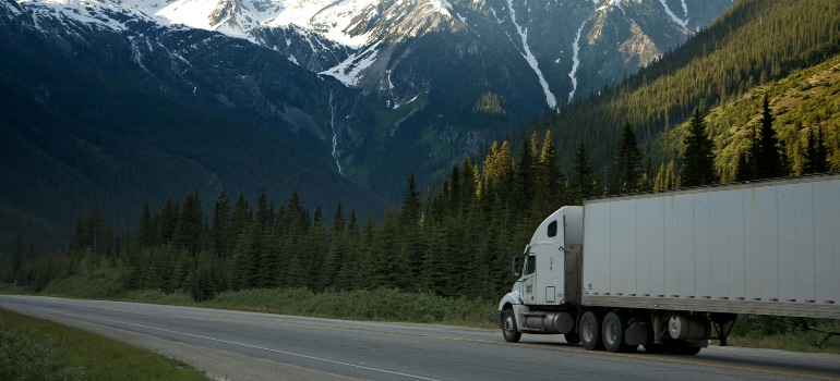 Long-distance moving truck driving through the mountains, showing the traits of reliable professional movers’ home for the first time.