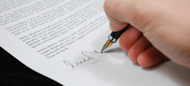 Person signing a moving contract, highlighting one of the key traits of reliable professional movers’ home for the first time.