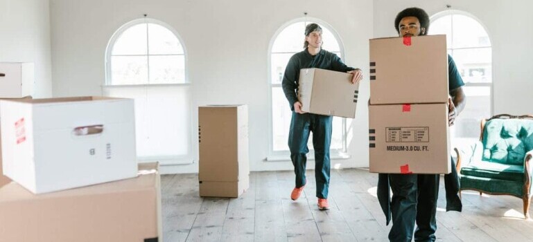 Two Centennial Moving professionals carrying moving boxes out of a client's home.