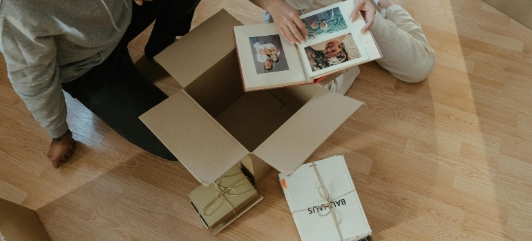 Two people sitting on the floor, flipping through an old photo album while unpacking boxes.