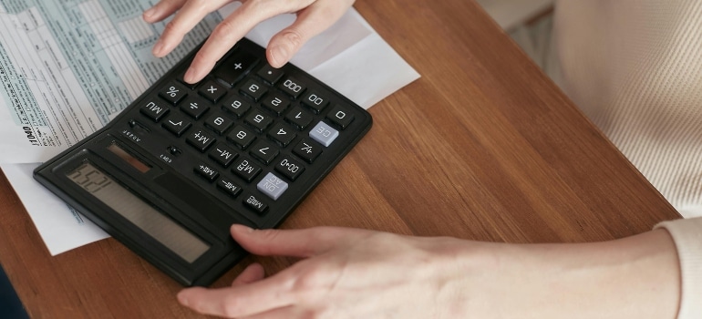 Hands using a calculator to budget costs for movers Prince Edward Island’ home for the first time.