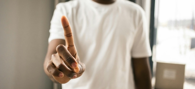Person in a white shirt holding up one finger as a warning or reminder.