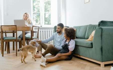 A family at home, with a father and daughter playing with their dog while the mother sits nearby, reflecting Vancouver real estate insights for new residents